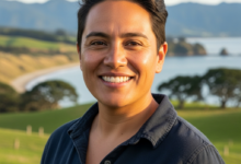 A photorealistic image showing a content person with a bright, healthy smile, set against a softly blurred backdrop of rolling green hills and a serene coastline, characteristic of the New Zealand landscape. The person's face is in sharp focus, conveying satisfaction and well-being.