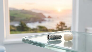 A close-up, photorealistic image of a high-tech dental implant and a ceramic crown on a glass surface, with a blurred background of a scenic New Zealand coastline, representing advanced dental care options.