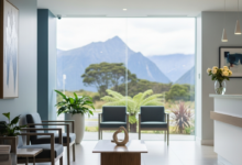 A clean, modern dental clinic waiting area with contemporary seating, bathed in soft natural light. Through a large, blurred window in the background, a serene natural landscape typical of New Zealand is subtly visible, emphasizing the location and readiness for urgent dental care.
