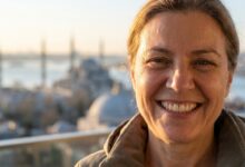 A close-up, photorealistic image of a happy mature person with a perfect smile, with the beautiful, blurred skyline of Istanbul and the Bosphorus visible in the background during a warm sunrise.