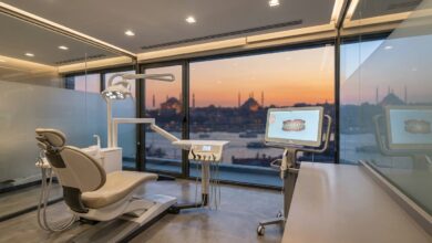 A pristine, modern dental clinic room with an empty patient chair in the foreground and a large window showing a blurred, scenic view of the Istanbul, Turkey skyline at sunset, symbolizing dental tourism.