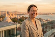 A close-up of a happy, confident person with a perfect white smile, standing on a balcony with a beautifully blurred background of the Istanbul, Turkey skyline at sunset.