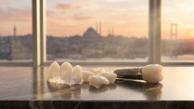 A close-up of perfect porcelain veneers and a dental implant model on a table in a luxury hotel room, with a beautifully blurred, scenic view of the Istanbul, Turkey skyline in the background at sunrise.