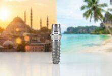 A pristine titanium dental implant is in sharp focus on a clean surface, with a split background showing a blurred Turkish city skyline on the left and a blurred Thai tropical beach on the right, symbolizing a choice.