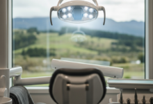 A serene and comforting view from a dental chair, looking up at a modern, soft-glowing dental light. Through a large window in the background, an extremely blurred, peaceful natural landscape hinting at New Zealand's scenery is visible. The clean environment and calming light emphasize relaxation and anxiety relief.