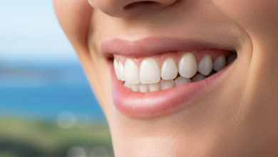 Close-up of a person's mouth showcasing a healthy, radiant smile with perfectly contoured pink gums and bright white teeth. The background is a soft, out-of-focus natural landscape, subtly hinting at New Zealand scenery.