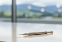 Close-up of a sterile, metallic dental instrument, like an endodontic file, resting on a clean white surface in a modern dental clinic, with a blurred, indistinct New Zealand landscape faintly visible through a distant window. The focus is sharp on the instrument, conveying precision and professionalism.
