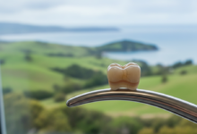 Close-up of a modern, natural-looking dental crown, showcasing its high-quality finish and material. In the out-of-focus background, a serene New Zealand landscape with green hills is softly visible, connecting the dental topic to the local context.