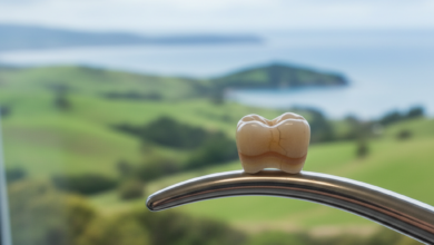 Close-up of a modern, natural-looking dental crown, showcasing its high-quality finish and material. In the out-of-focus background, a serene New Zealand landscape with green hills is softly visible, connecting the dental topic to the local context.