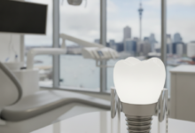 A photorealistic image of a sleek, modern dental clinic interior. In the foreground, there's an abstract, gleaming white dental implant or tooth model. Through a blurred window in the background, the iconic Auckland city skyline and harbor are visible. The scene is bright, clean, and professionally lit.